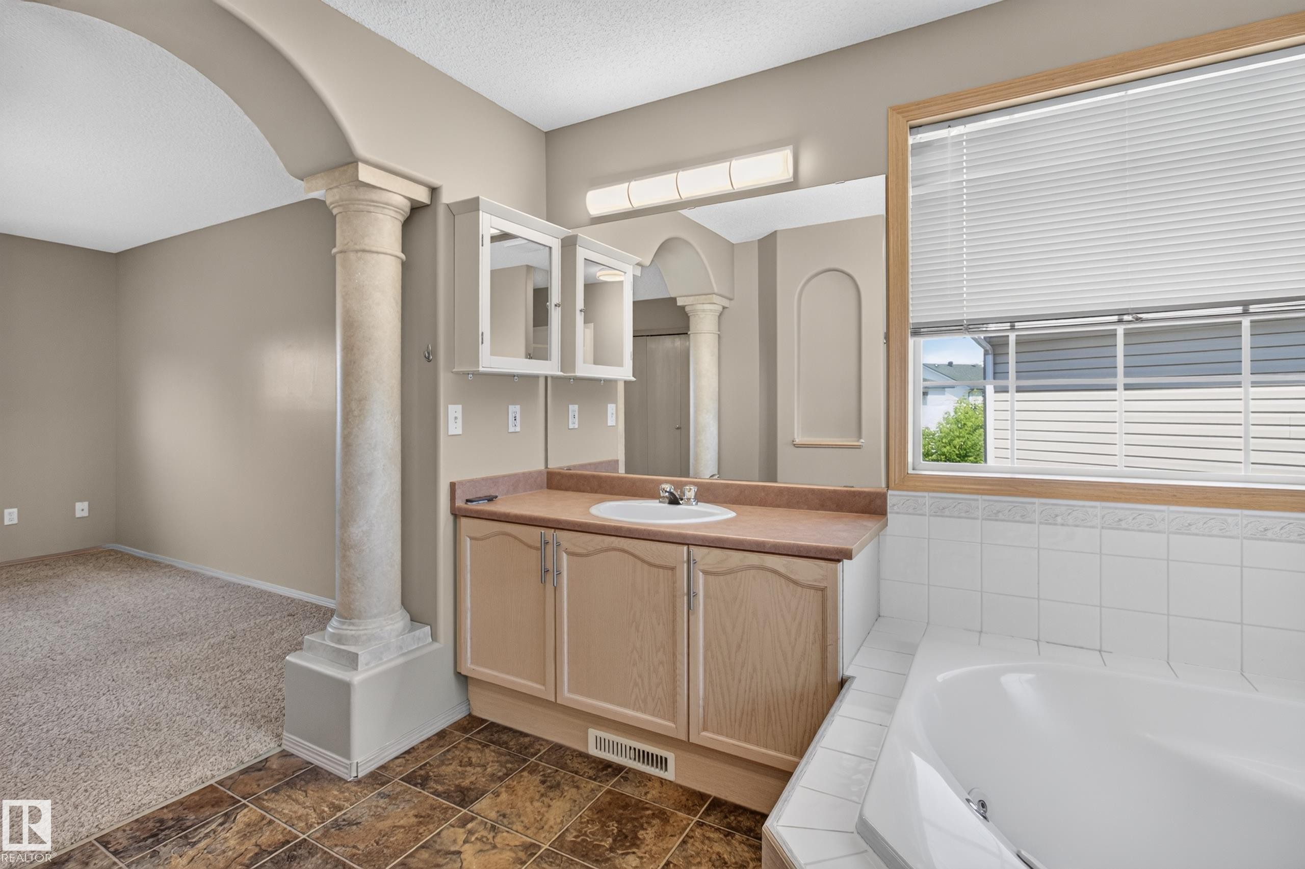 Bathroom vanity featuring a single basin sink, light wood-finish cabinetry, and a large mirror - 13406 32A Street, Edmonton, AB