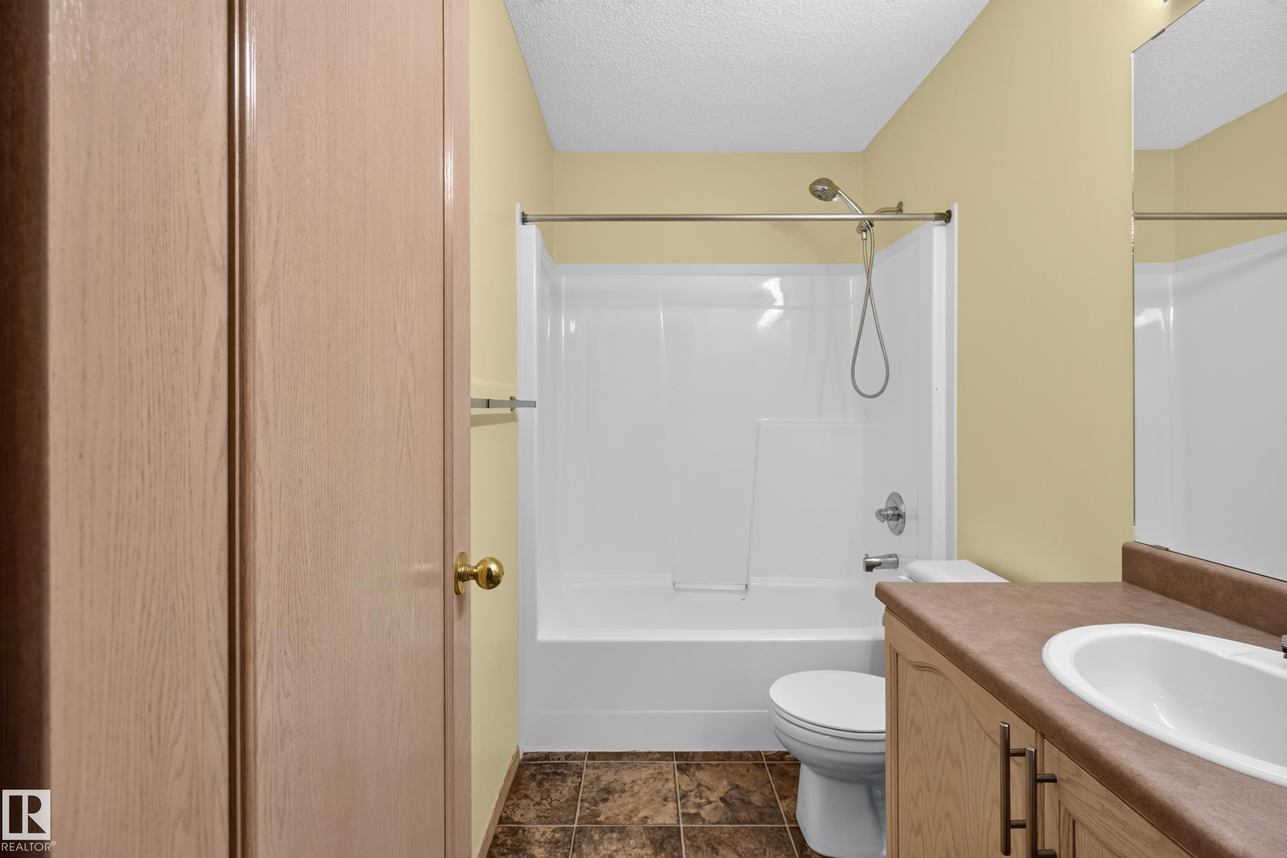 Bathroom featuring a white tub/shower combination, light wood-finish vanity with an integrated sink, and patterned flooring - 13406 32A Street, Edmonton, AB