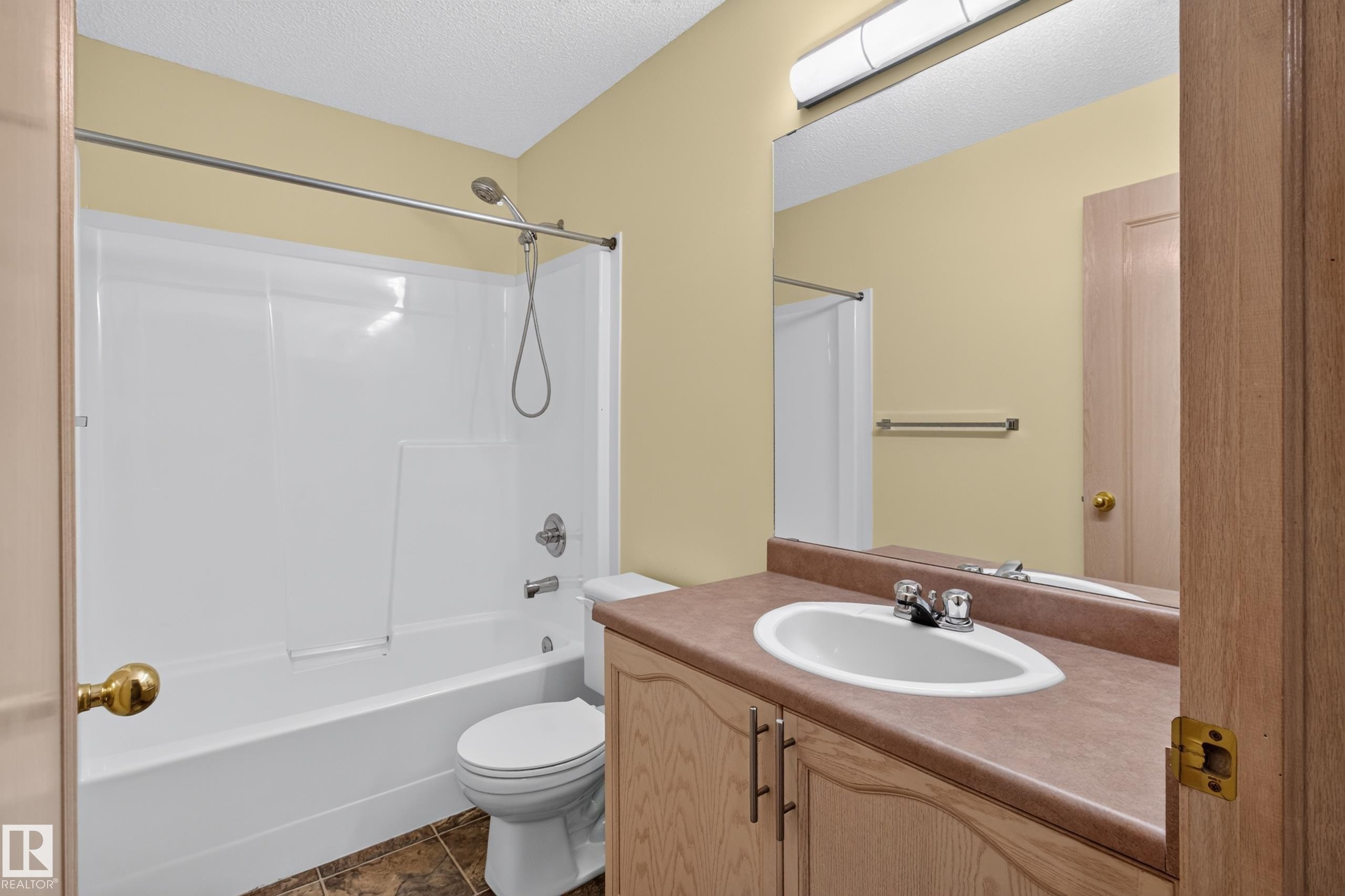 Bathroom featuring a white bathtub and shower surround, chrome fixtures, a vanity with a laminate countertop, and wood-finish cabinetry - 13406 32A Street, Edmonton, AB