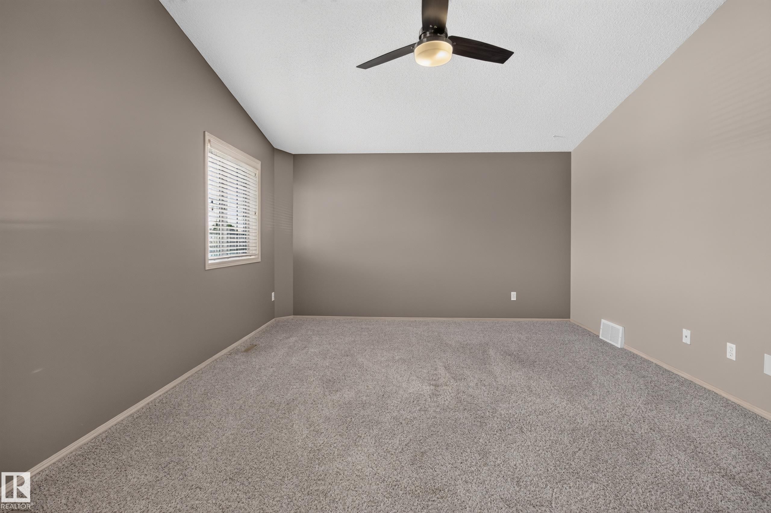 Spacious room featuring neutral wall tones, textured ceiling, a window with horizontal blinds, and a dark-toned ceiling fan - 13406 32A Street, Edmonton, AB