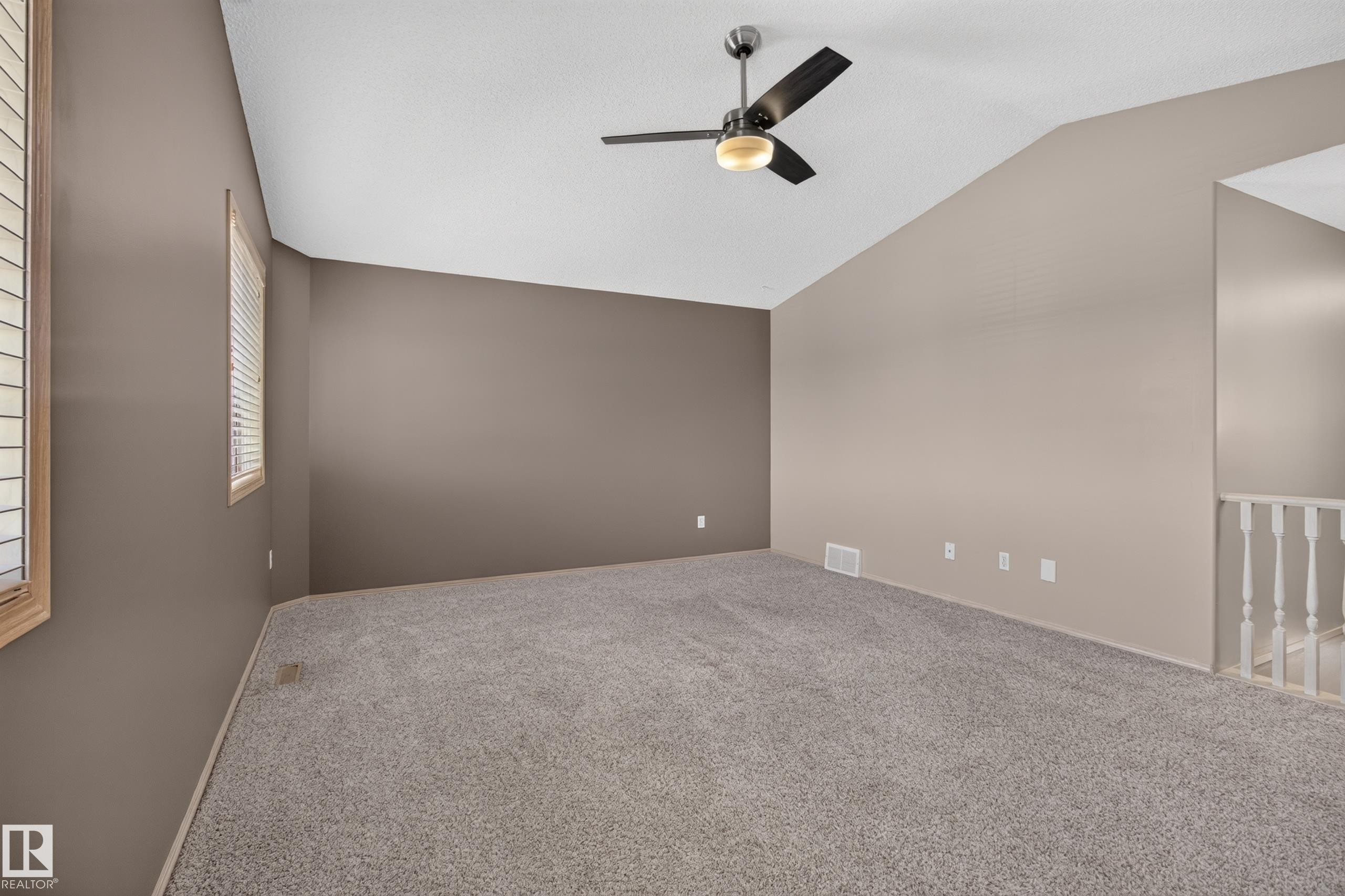 Spacious room featuring vaulted ceilings, a ceiling fan with integrated lighting, two windows with blinds, and neutral-toned carpeting - 13406 32A Street, Edmonton, AB