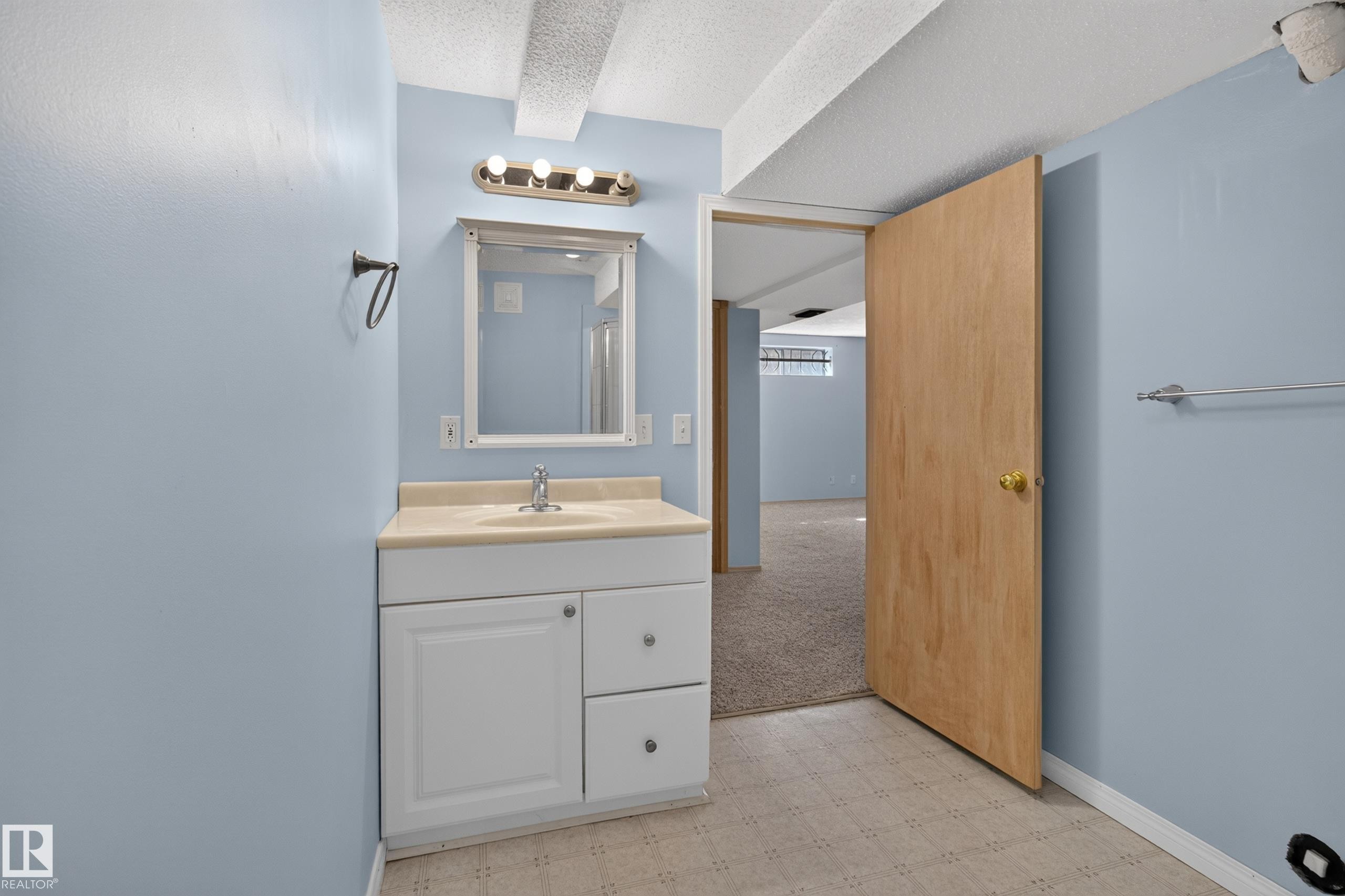 Bathroom featuring a single vanity with a countertop, integrated sink, and white cabinetry - 13406 32A Street, Edmonton, AB
