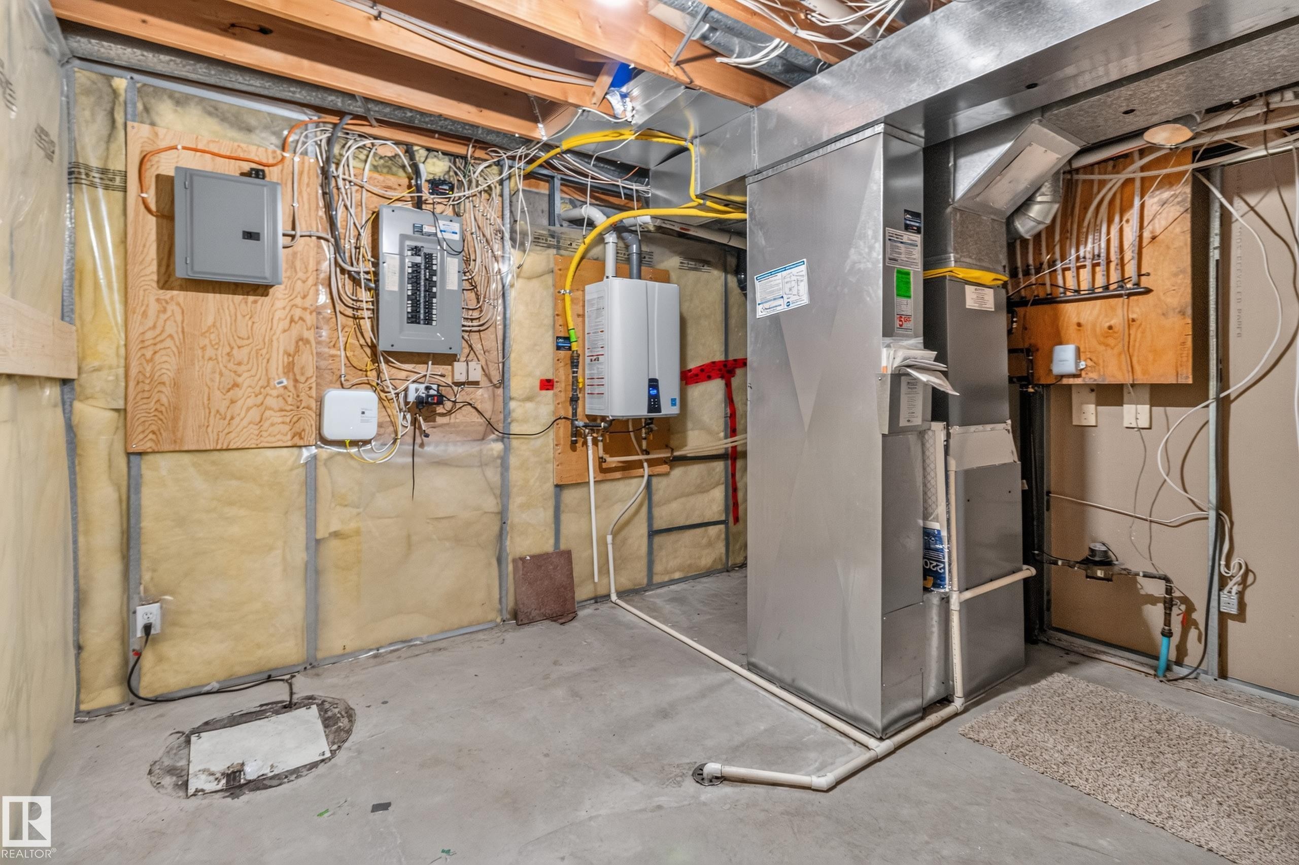 Basement utility area featuring exposed joist ceiling, concrete flooring, a tankless water heater, and a furnace unit - 13406 32A Street, Edmonton, AB