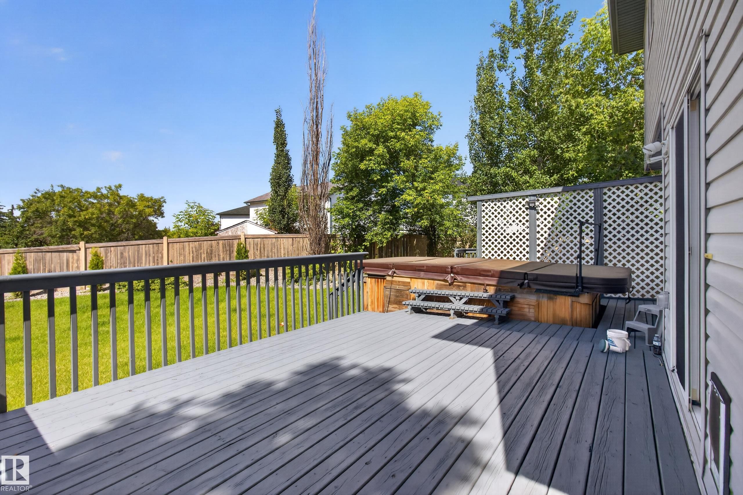 Spacious outdoor deck with a dark grey finish, featuring an integrated hot tub with wooden surround, and a white lattice privacy screen - 13406 32A Street, Edmonton, AB