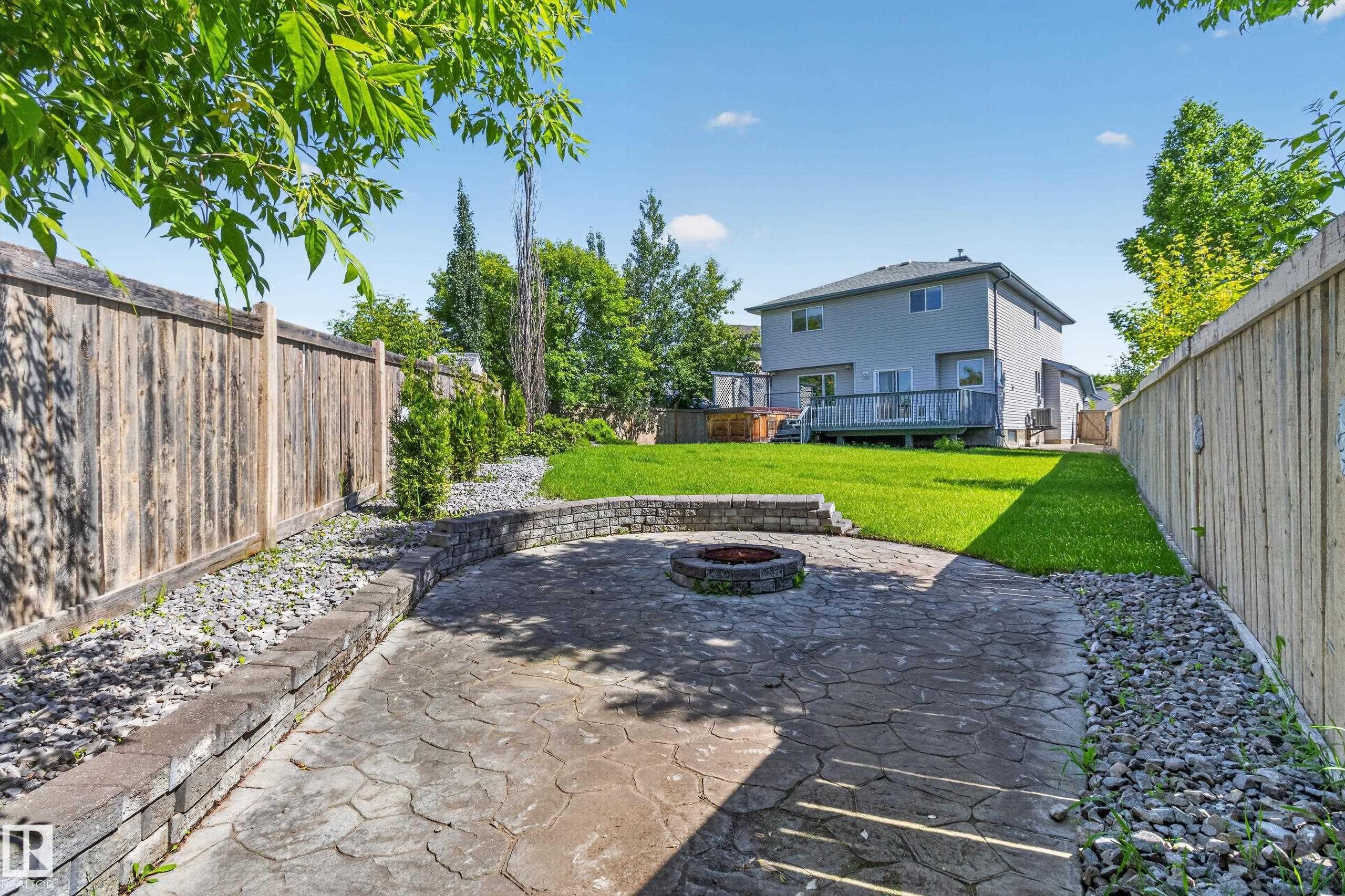 Expansive backyard featuring a stamped concrete patio with a built-in fire pit, a stone retaining wall, and a large manicured lawn - 13406 32A Street, Edmonton, AB