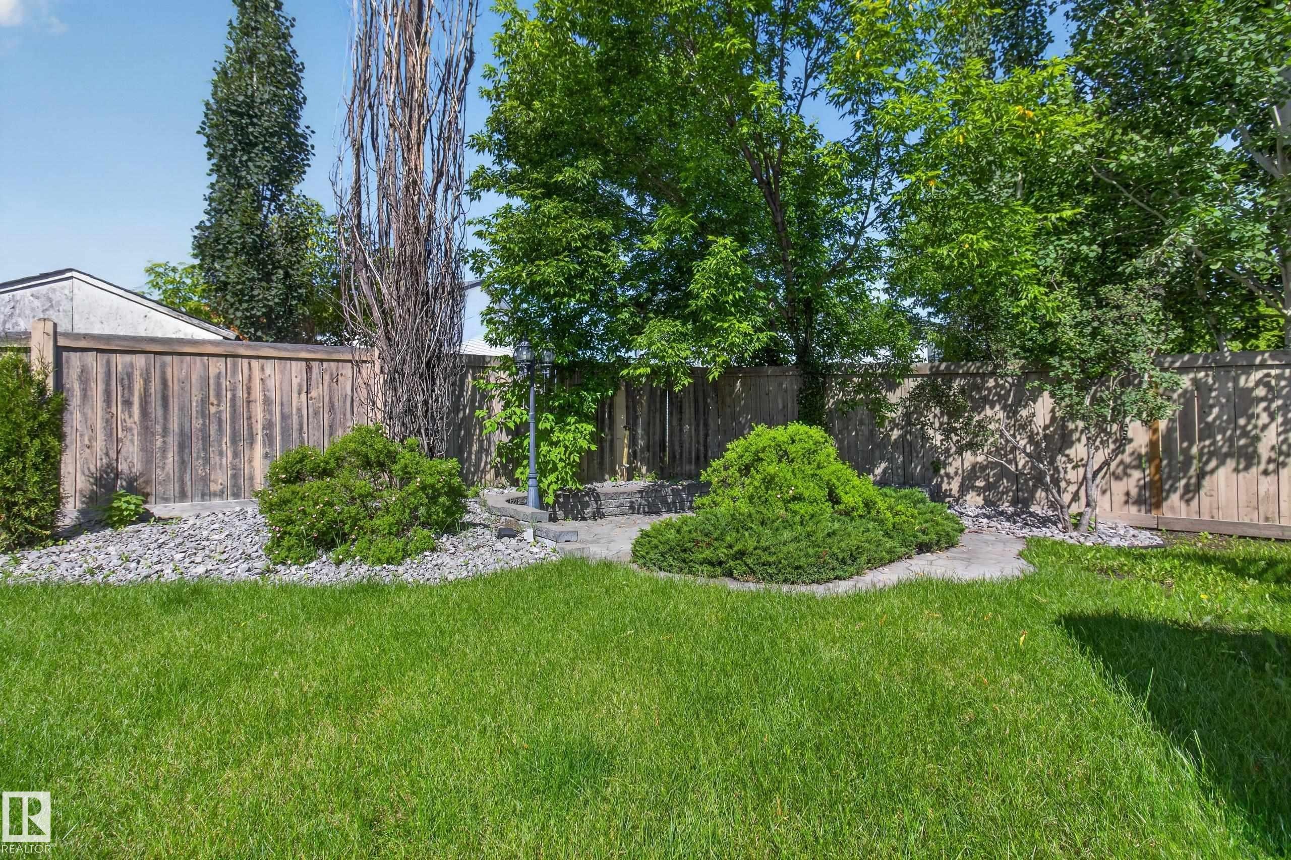 Expansive lawn with natural wood fencing, mature trees, and decorative shrubbery - 13406 32A Street, Edmonton, AB