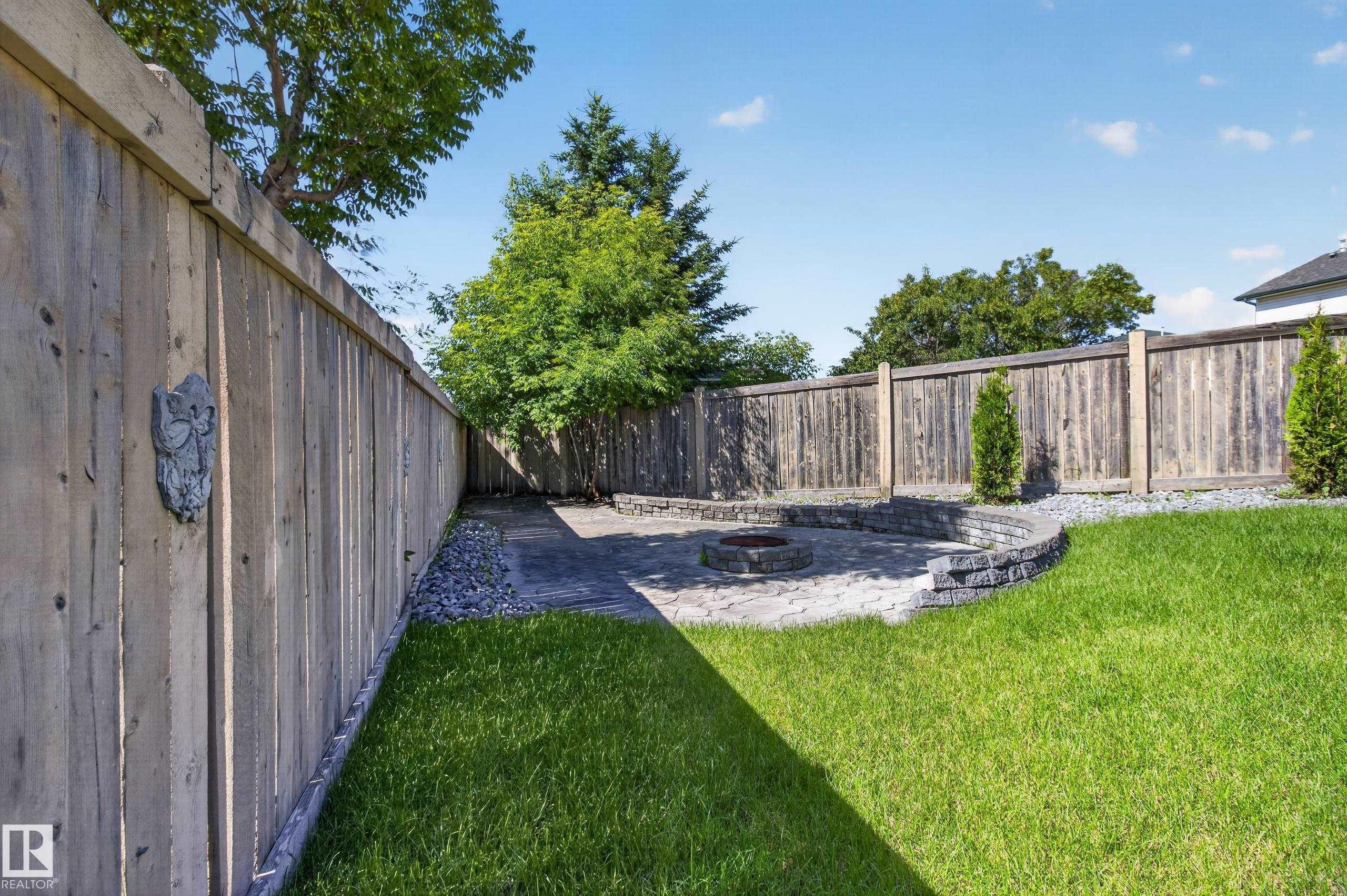 Expansive fenced backyard featuring a stone fire pit, curved stone retaining walls, and a paver patio - 13406 32A Street, Edmonton, AB