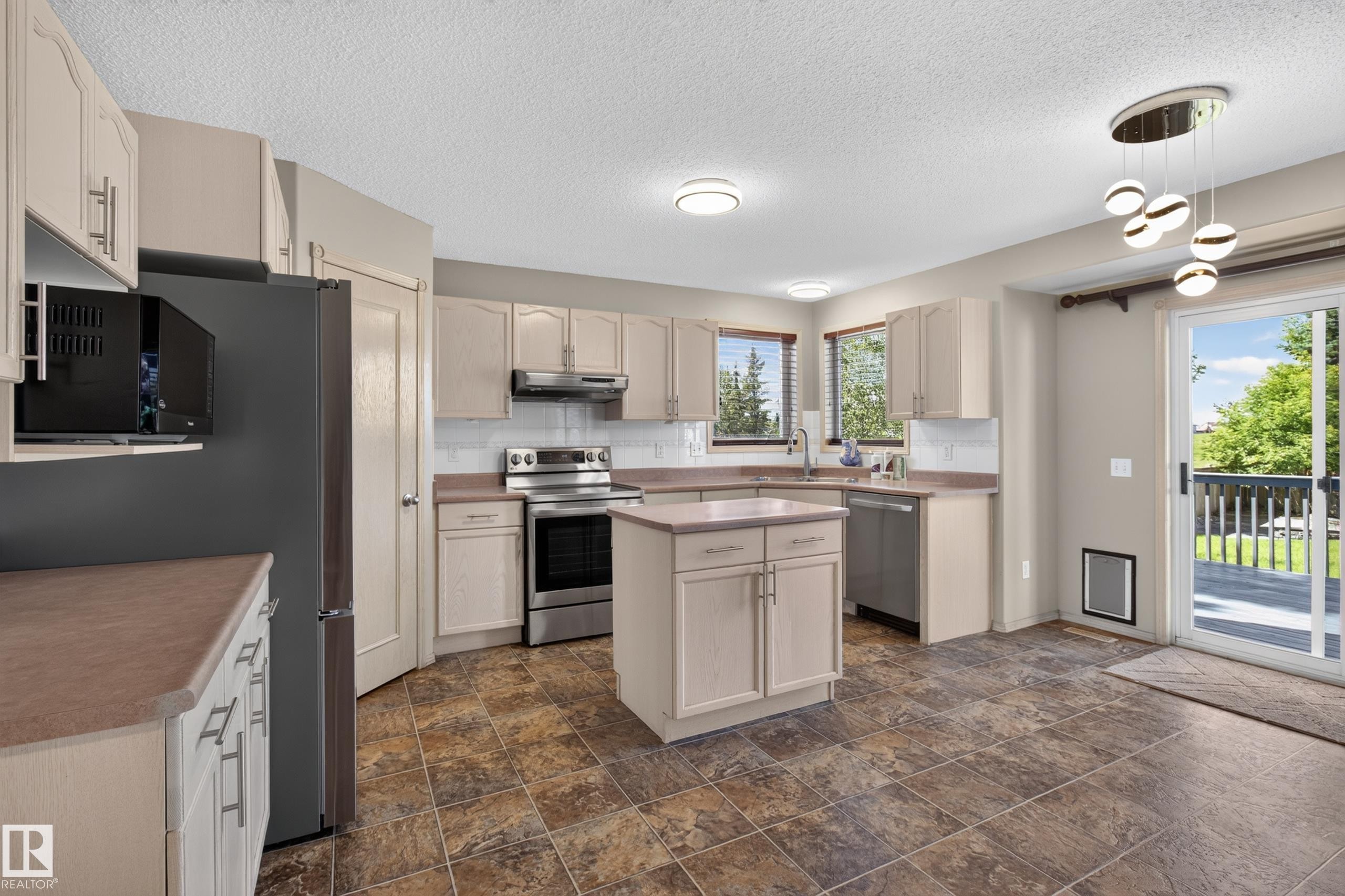 Kitchen featuring light-toned cabinetry with T-bar handles, stainless steel appliances, a central island, and wood-finish flooring - 13406 32A Street, Edmonton, AB