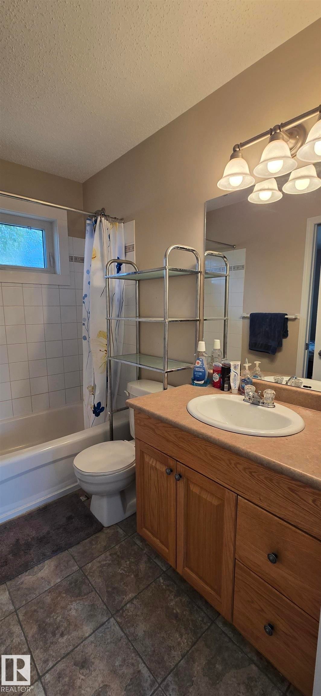 Bathroom featuring a single vanity with wood-finish cabinetry, an integrated sink, and a large wall-mounted mirror - 4734 54A Avenue, Vegreville, AB - Indoor Photo Showing Bathroom
