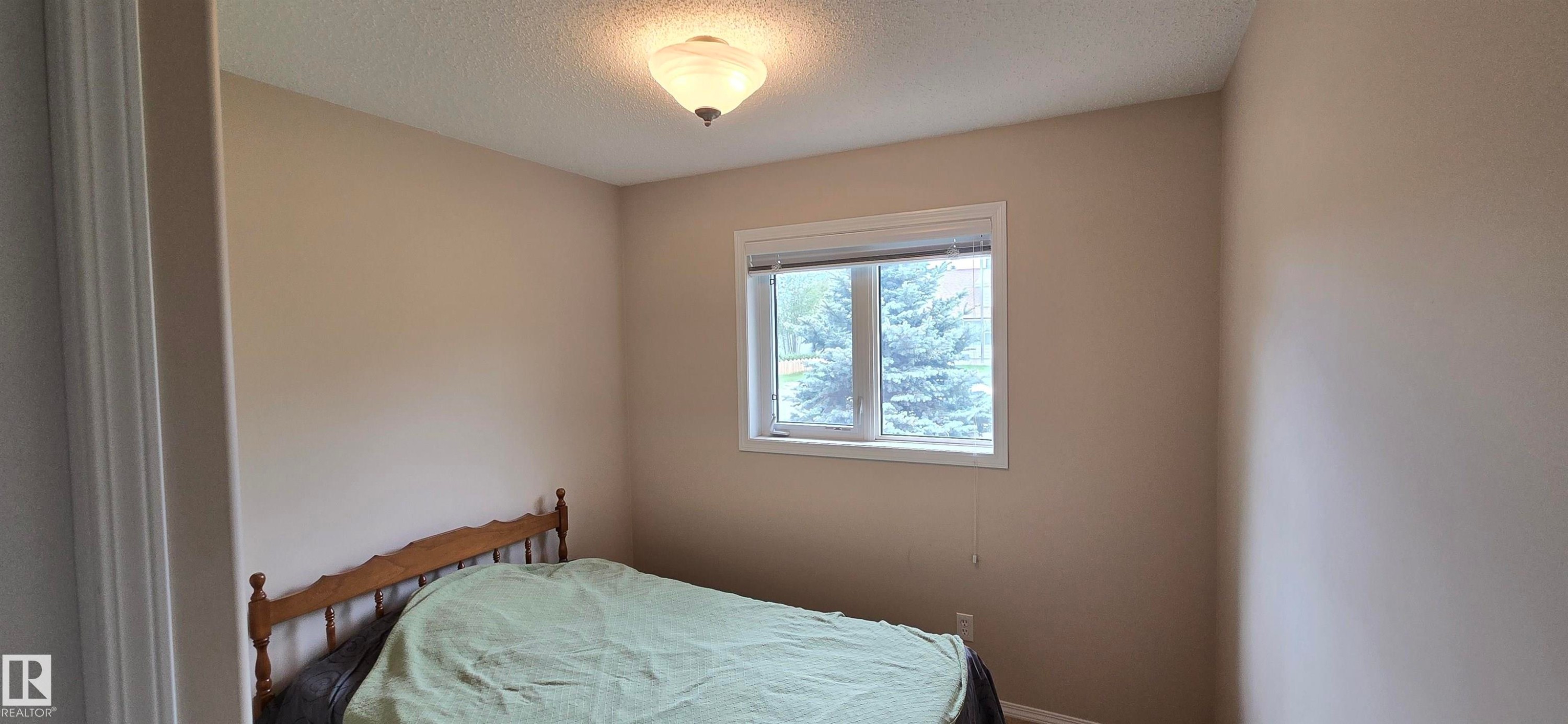 Neutral-toned room featuring a single window with white trim, a flush-mount ceiling light fixture, and textured ceilings - 4734 54A Avenue, Vegreville, AB - Indoor Photo Showing Bedroom