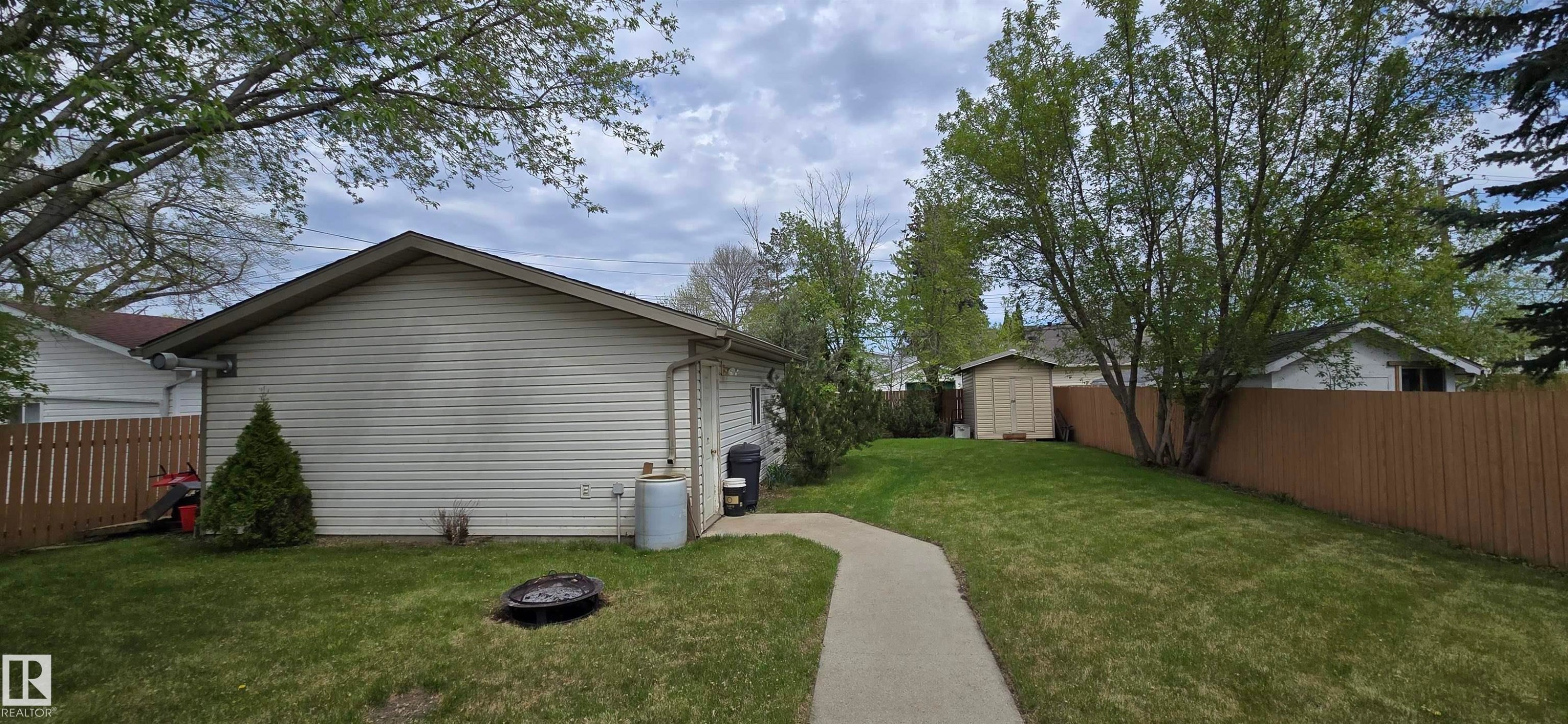 Expansive backyard featuring a manicured lawn, established trees, and a concrete pathway - 4734 54A Avenue, Vegreville, AB - Outdoor