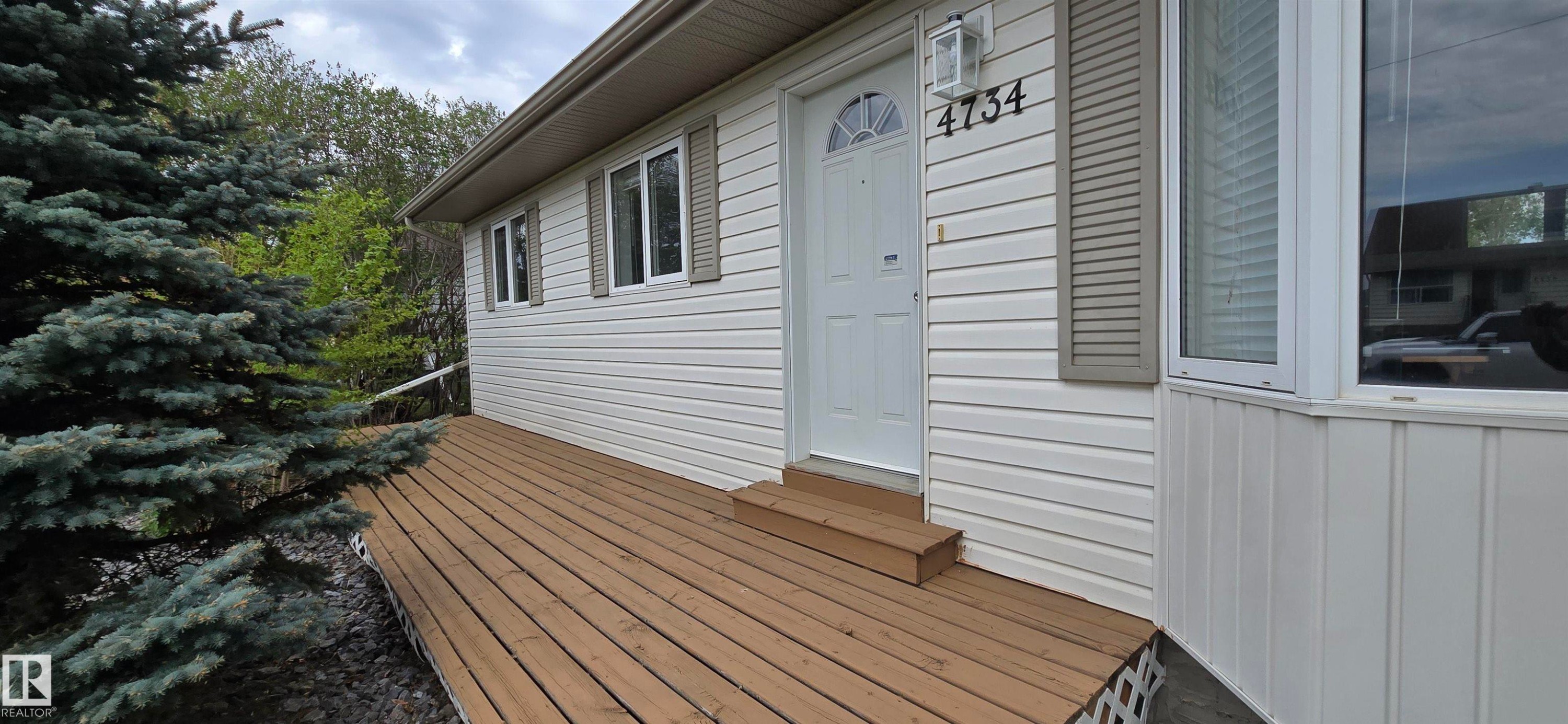 Expansive wood deck with a two-step entry, white vinyl siding, decorative window shutters, and a prominent bay window - 4734 54A Avenue, Vegreville, AB - Outdoor With Exterior