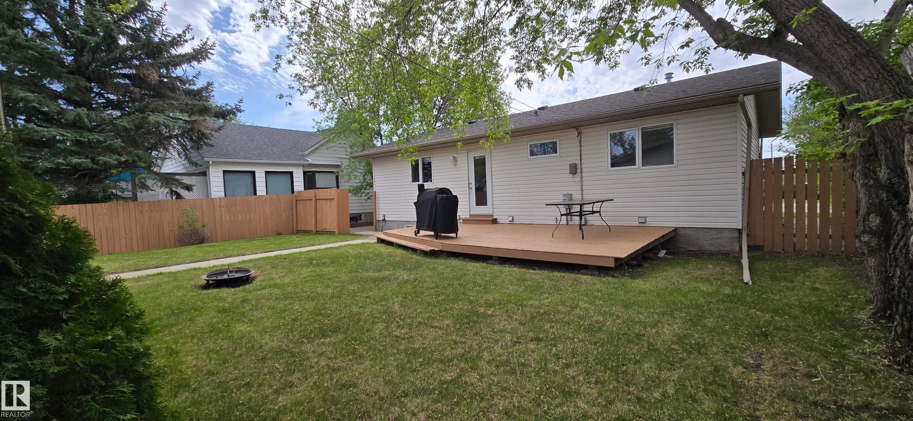 Expansive rear yard featuring a large composite deck, perimeter wood fencing, and mature trees - 4734 54A Avenue, Vegreville, AB - Outdoor With Deck Patio Veranda