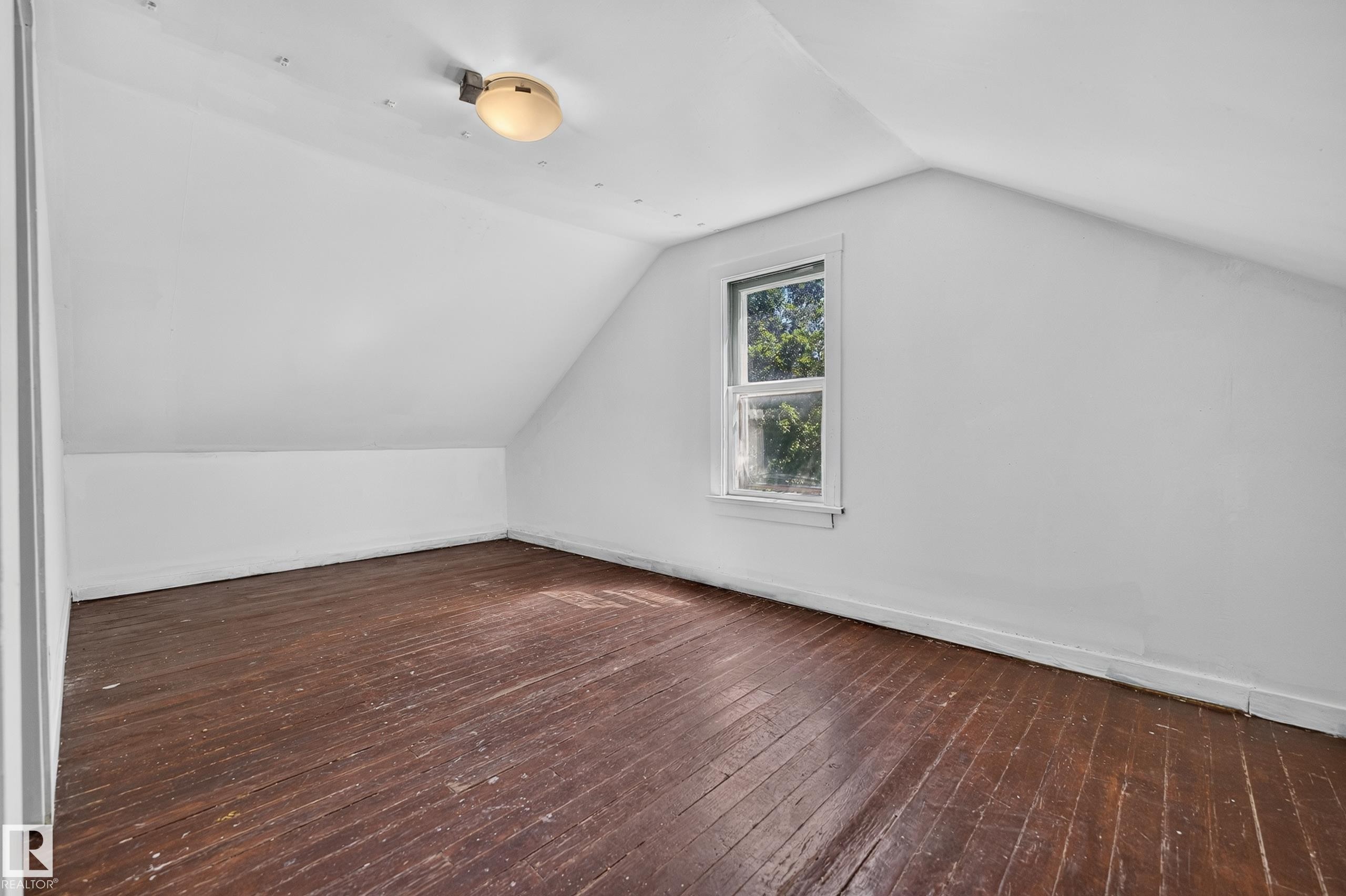 Interior room featuring a single window, sloped ceilings, and wood-finish flooring - 11708 79 Street, Edmonton, AB