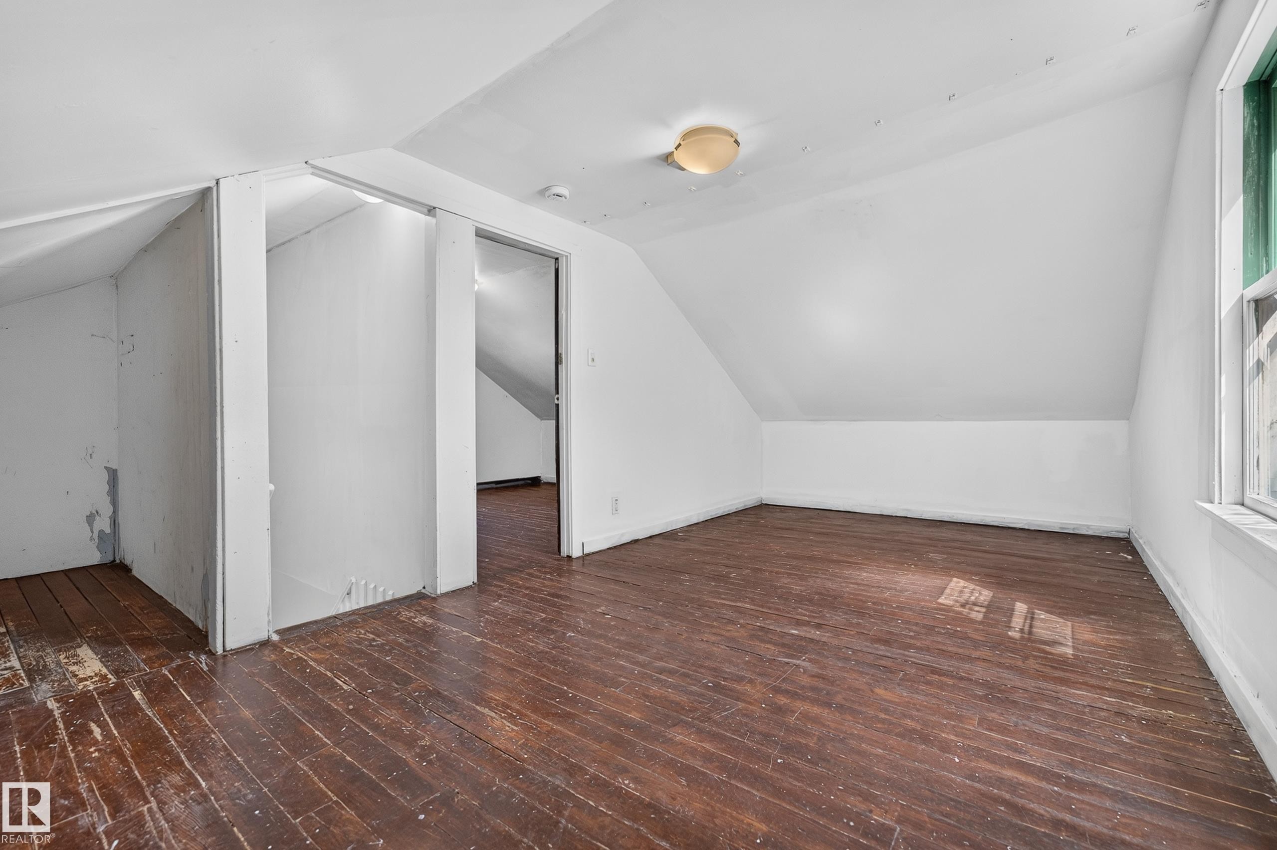 Room featuring wood-finish flooring, sloped ceilings, and a window with green trim - 11708 79 Street, Edmonton, AB