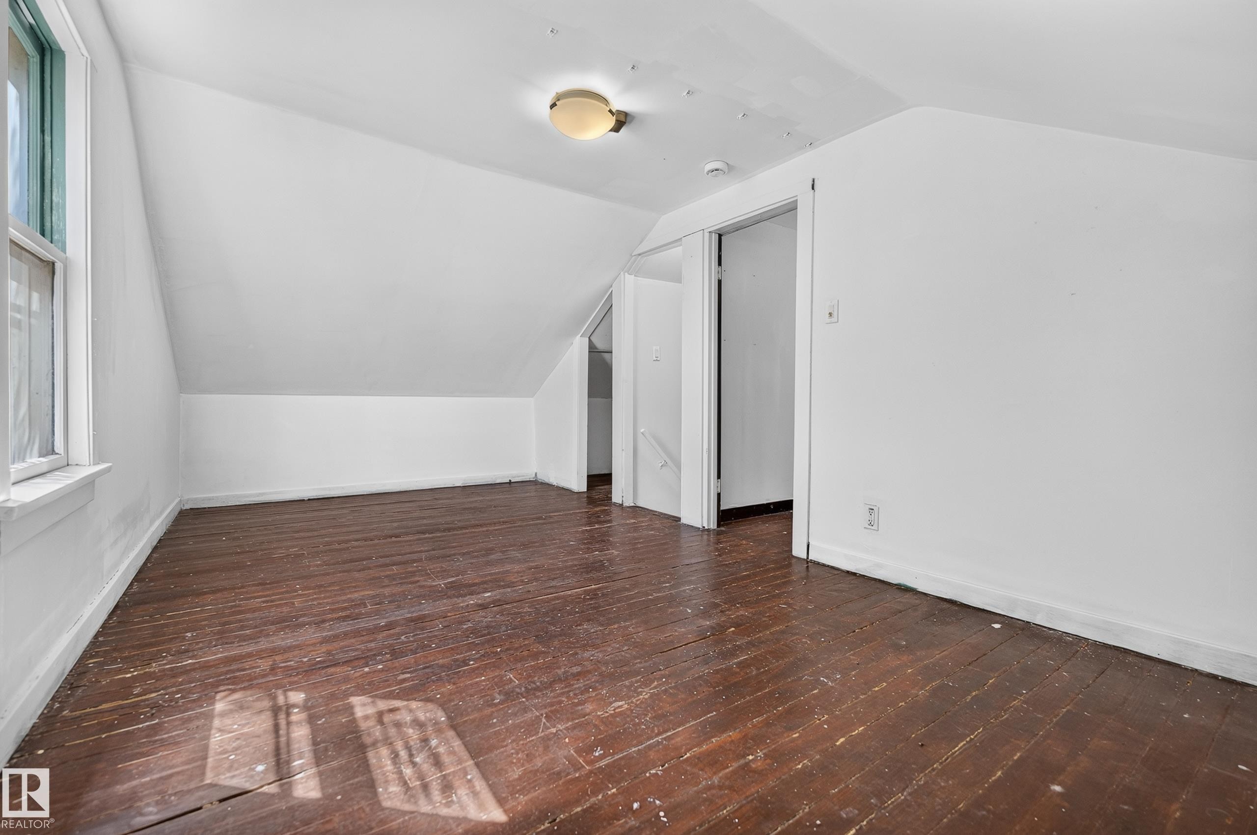 Attic space featuring sloped ceilings, a single-pane window, wood-finish flooring, and a flush-mount ceiling light - 11708 79 Street, Edmonton, AB