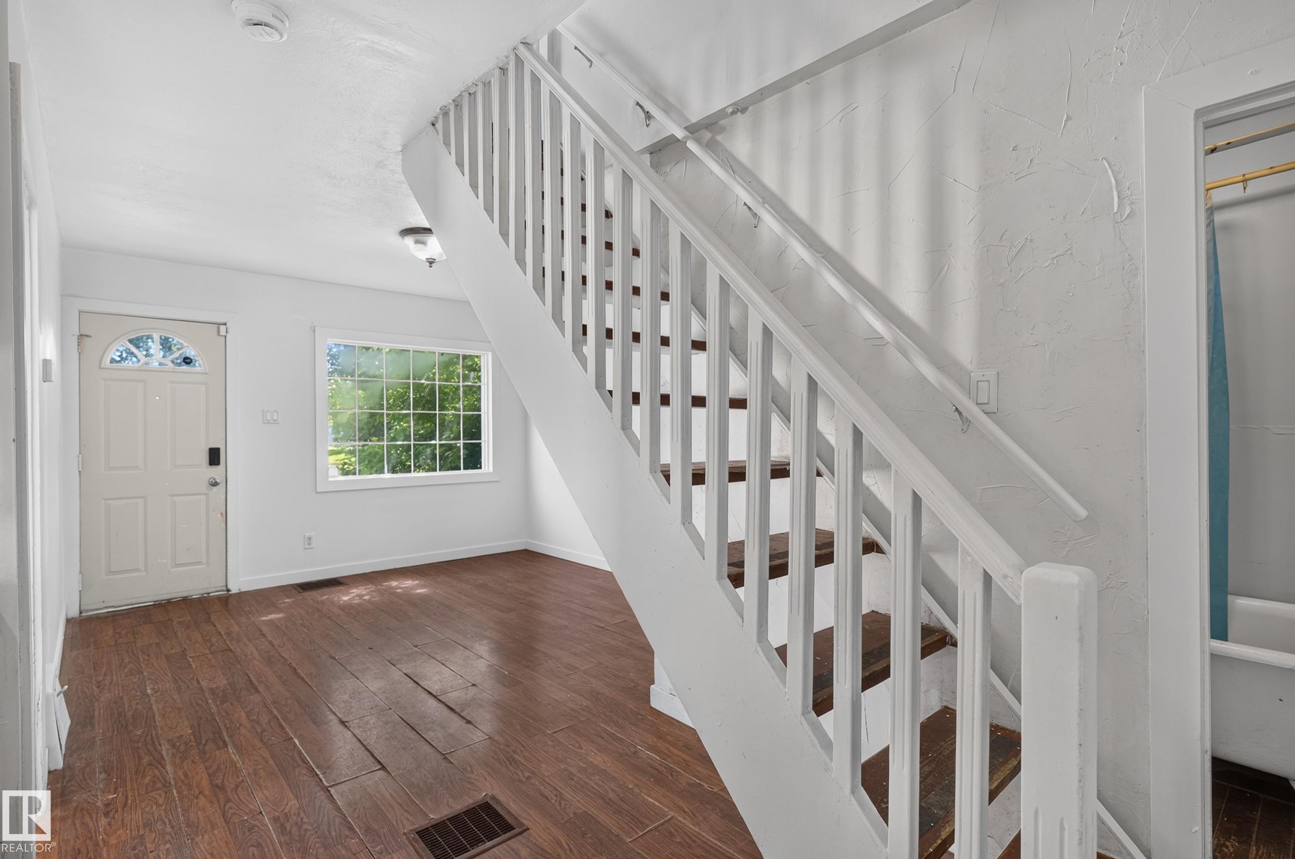 Staircase with white balusters and wood-finish treads, complemented by dark wood-finish flooring - 11708 79 Street, Edmonton, AB