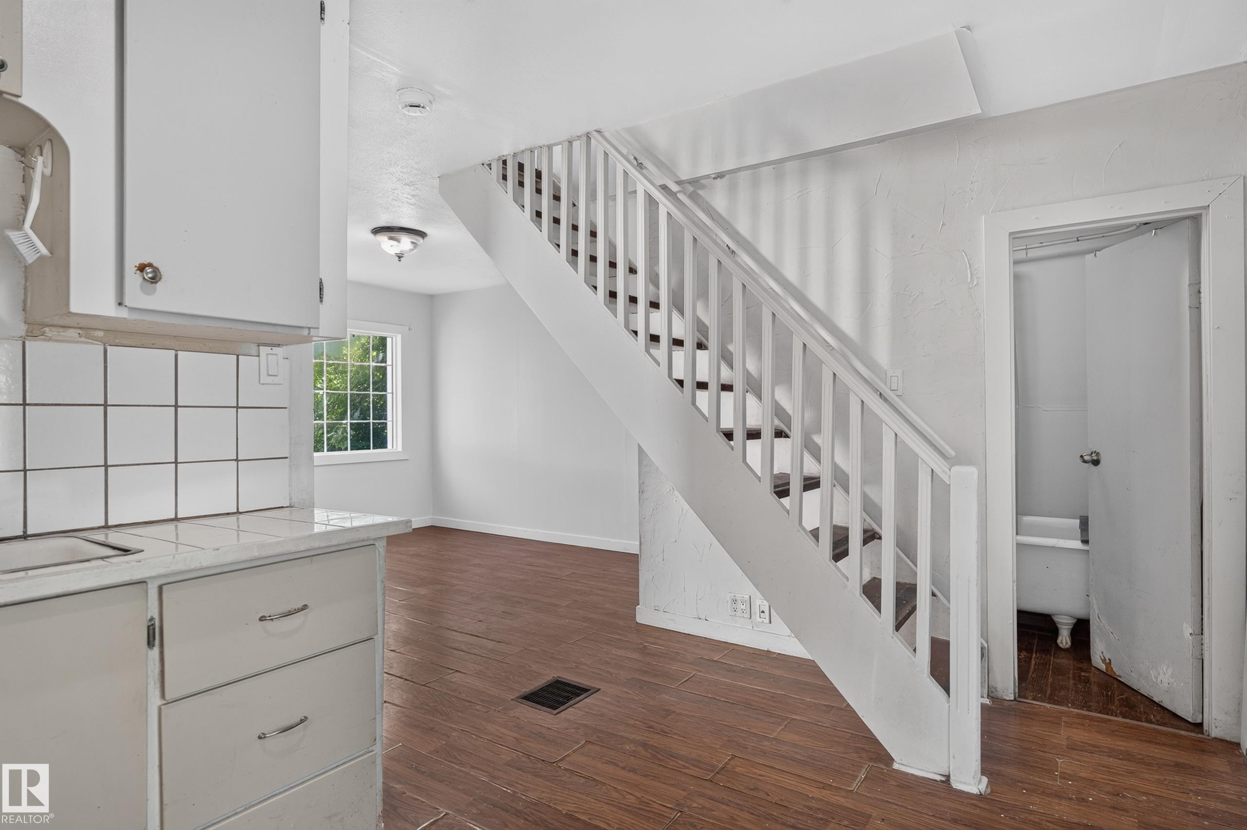 White painted staircase with wood-finish treads, leading from a room featuring wood-finish flooring and a white tile backsplash - 11708 79 Street, Edmonton, AB