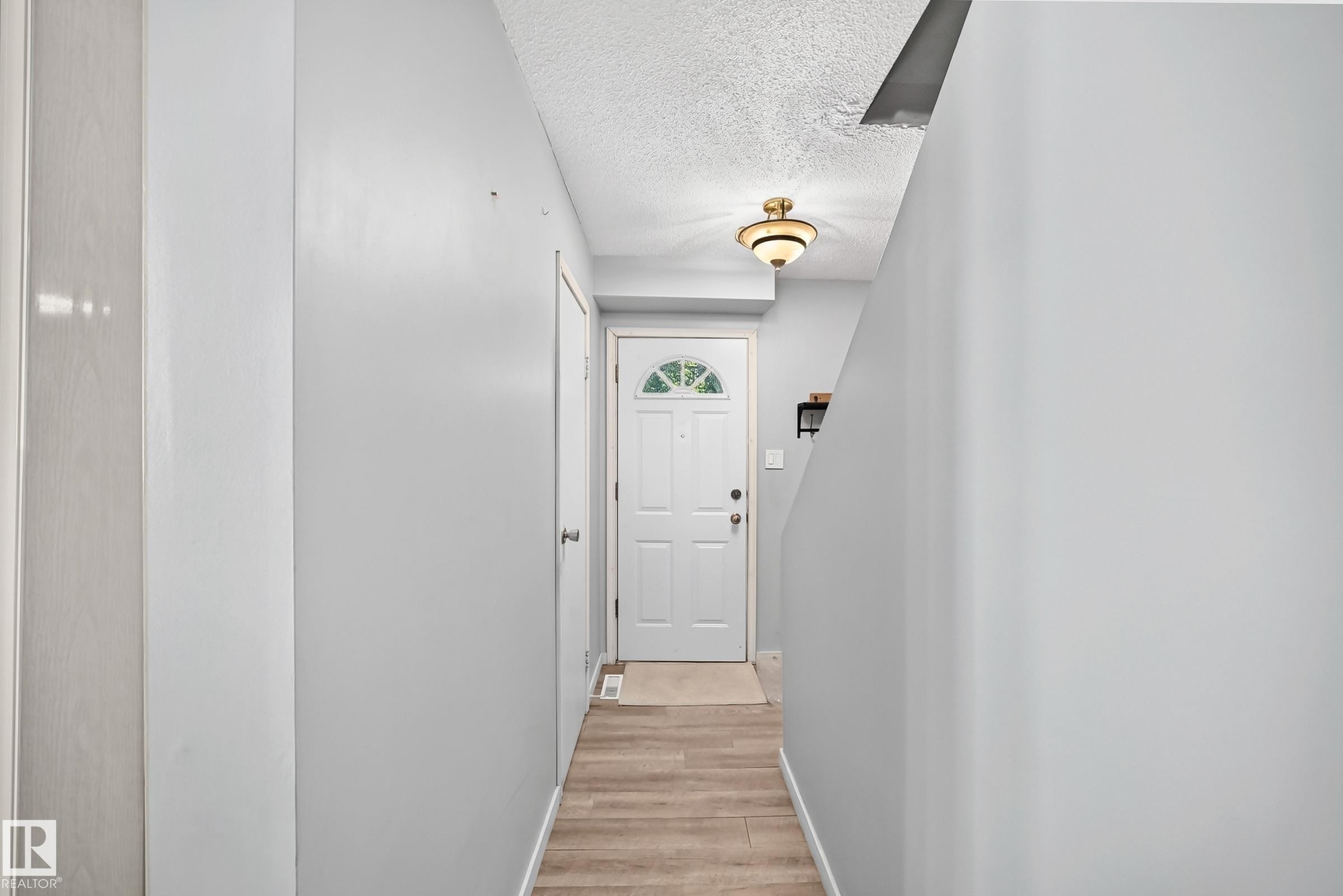 Entryway featuring wood-finish flooring, a white paneled door with an arched window, and a flush-mount light fixture - 355 Northgate Terrace, Edmonton, AB