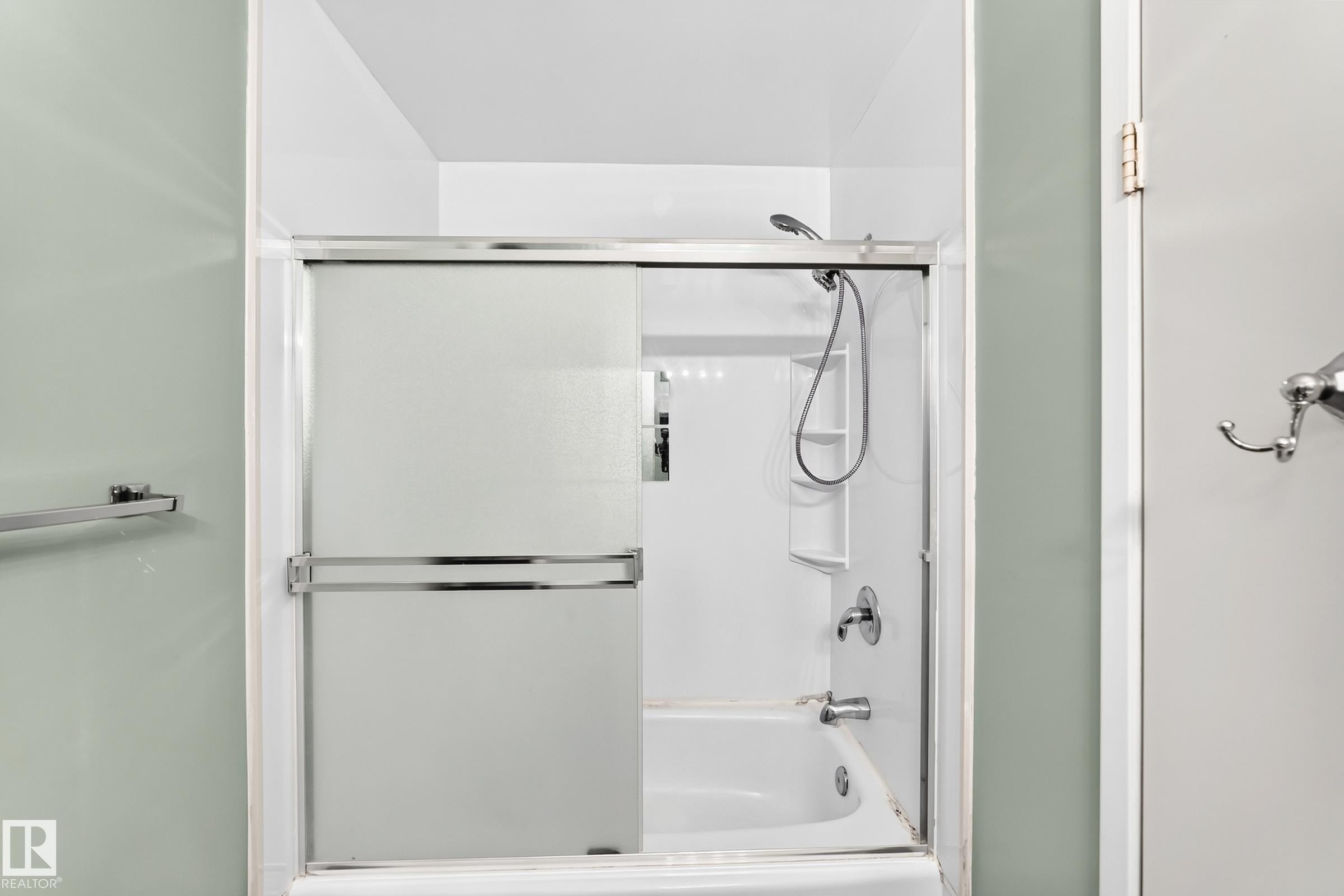 Bathtub with sliding glass enclosure featuring a chrome frame, integrated shelving, and a handheld showerhead - 355 Northgate Terrace, Edmonton, AB