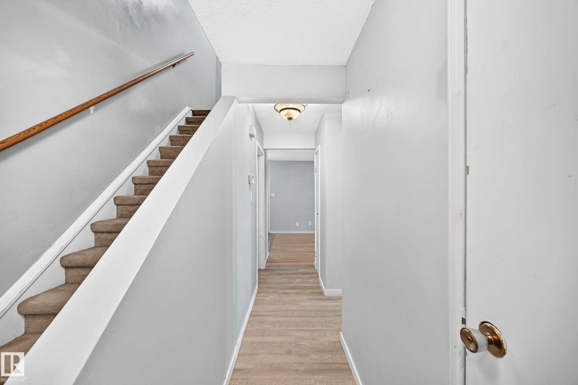 Carpeted staircase with a wood-finish handrail, light gray wall paint, and wood-finish flooring extending through the hallway - 355 Northgate Terrace, Edmonton, AB
