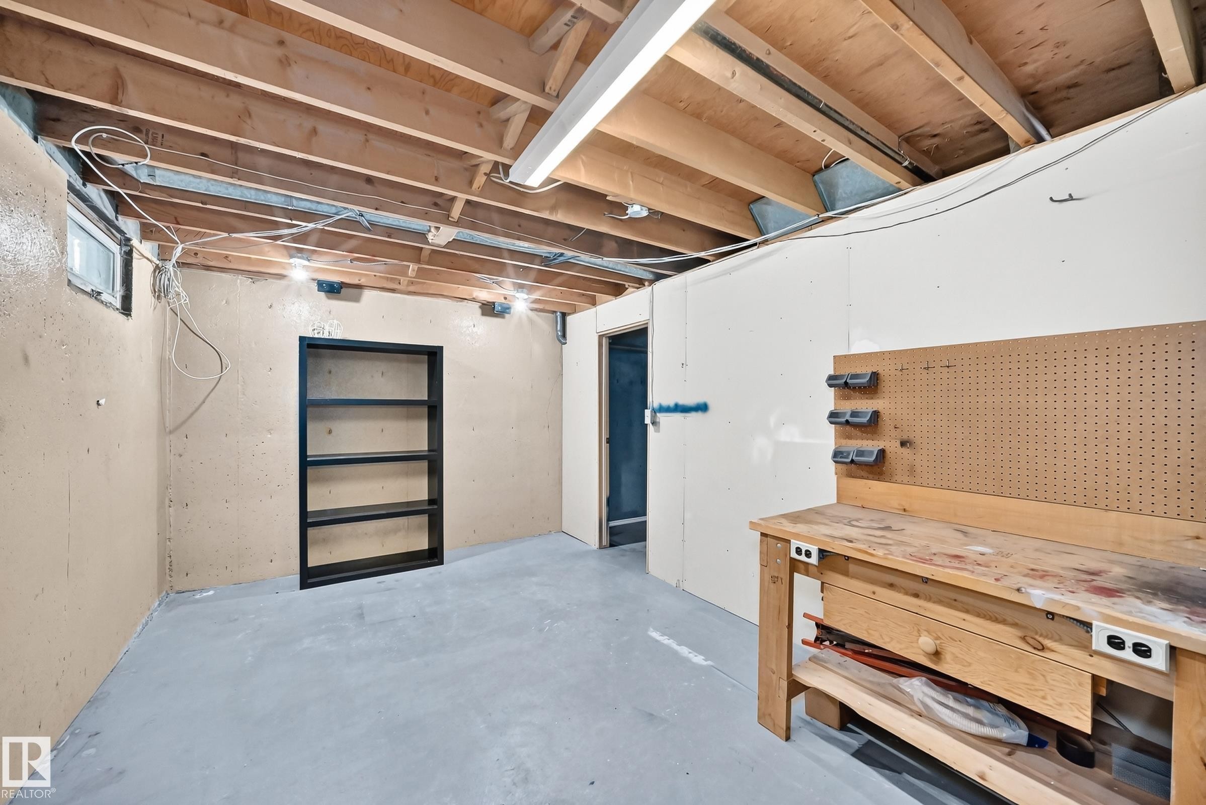 Unfinished basement space featuring exposed wood joists, concrete flooring, and a built-in workbench with pegboard - 355 Northgate Terrace, Edmonton, AB