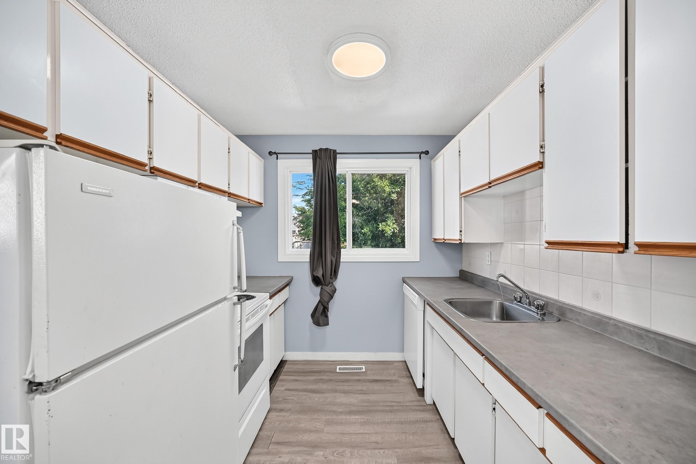 Galley kitchen featuring white cabinetry, light gray countertops, white tiled backsplash, a stainless steel sink, and wood-finish flooring - 355 Northgate Terrace, Edmonton, AB