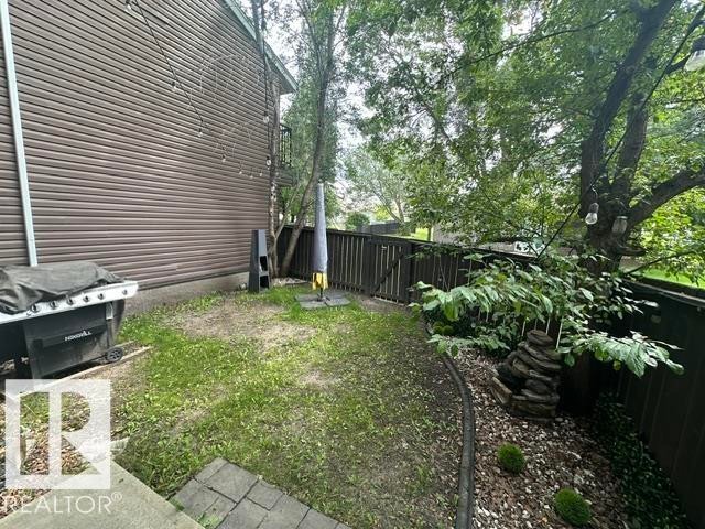 Private backyard featuring a slatted privacy fence, mature trees, and a decorative rock feature - 18020 96 Avenue, Edmonton, AB