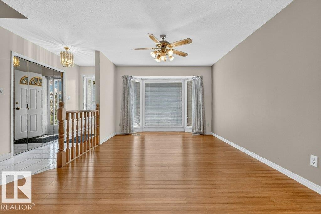 Open-concept living area featuring wood-finish flooring, a bay window with drapes, and a ceiling fan with integrated lighting - 16524 99 Street Nw, Edmonton, AB - Indoor Photo Showing Other Room