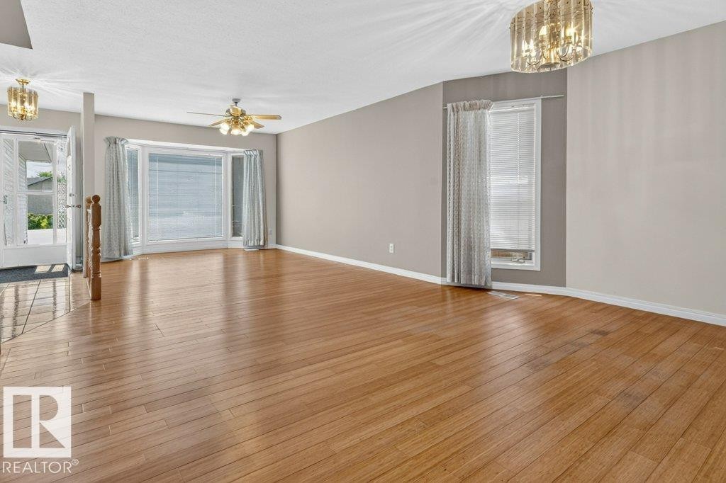 Spacious interior featuring wood-finish flooring, neutral wall paint, and a bay window with blinds - 16524 99 Street Nw, Edmonton, AB - Indoor