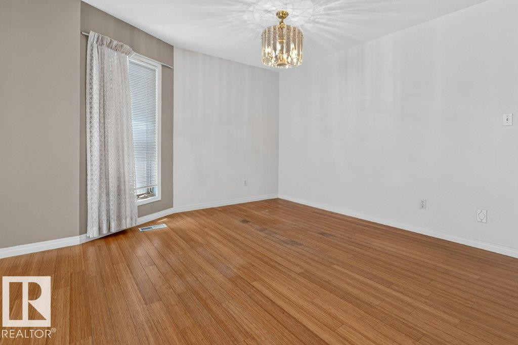 Room featuring wood-finish flooring, a contemporary crystal chandelier, and a window with blinds and drapes - 16524 99 Street Nw, Edmonton, AB - Indoor Photo Showing Other Room