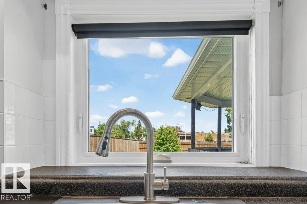 Kitchen sink with a high-arc gooseneck faucet, integrated soap dispenser, and a dark speckled countertop - 16524 99 Street Nw, Edmonton, AB - Indoor