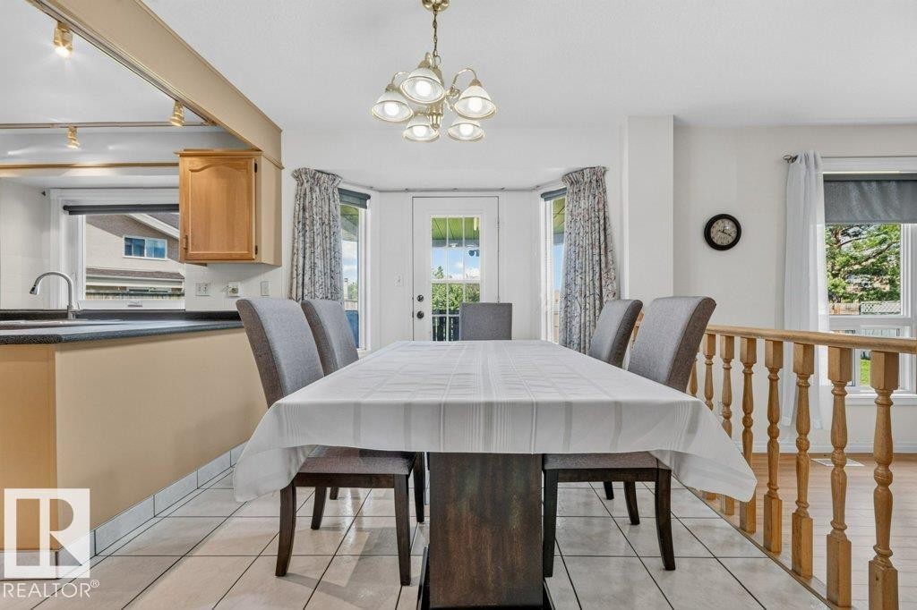 Dining space featuring a suspended chandelier, bay windows with an exterior door, and tile flooring - 16524 99 Street Nw, Edmonton, AB - Indoor Photo Showing Dining Room