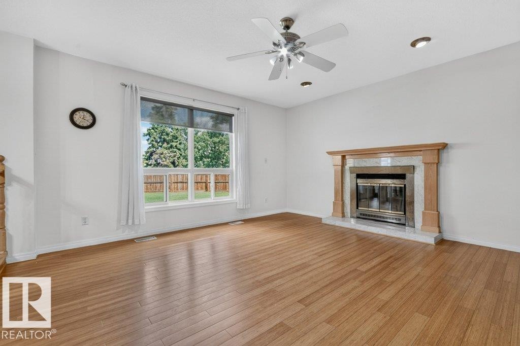 Spacious room featuring wood-finish flooring, a contemporary fireplace with a stone surround and wood mantel, a large window, a ceiling fan with integrated lighting, and recessed lighting - 16524 99 Street Nw, Edmonton, AB - Indoor Photo Showing Living Room With Fireplace