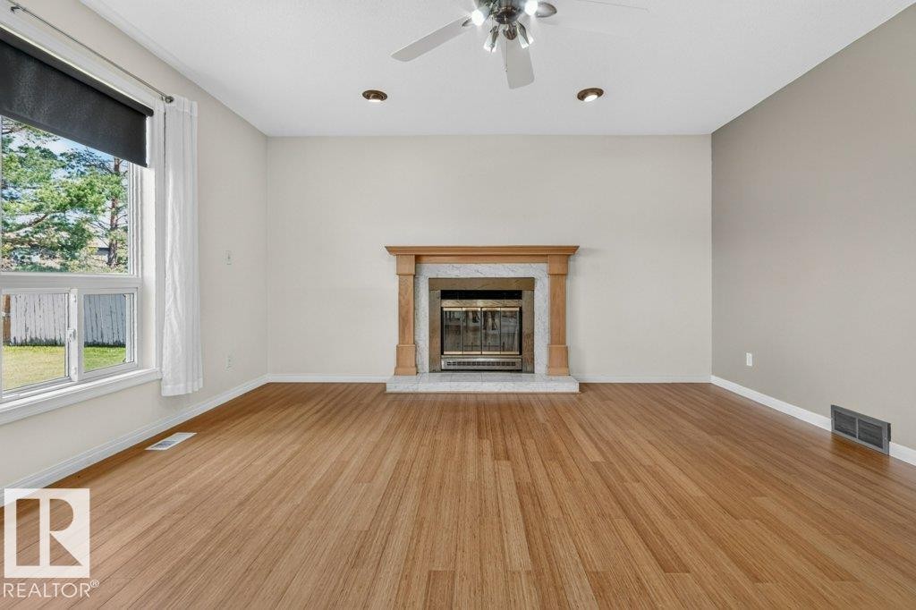 Living area featuring a central fireplace with a wood-finish mantel and stone surround - 16524 99 Street Nw, Edmonton, AB - Indoor Photo Showing Living Room With Fireplace