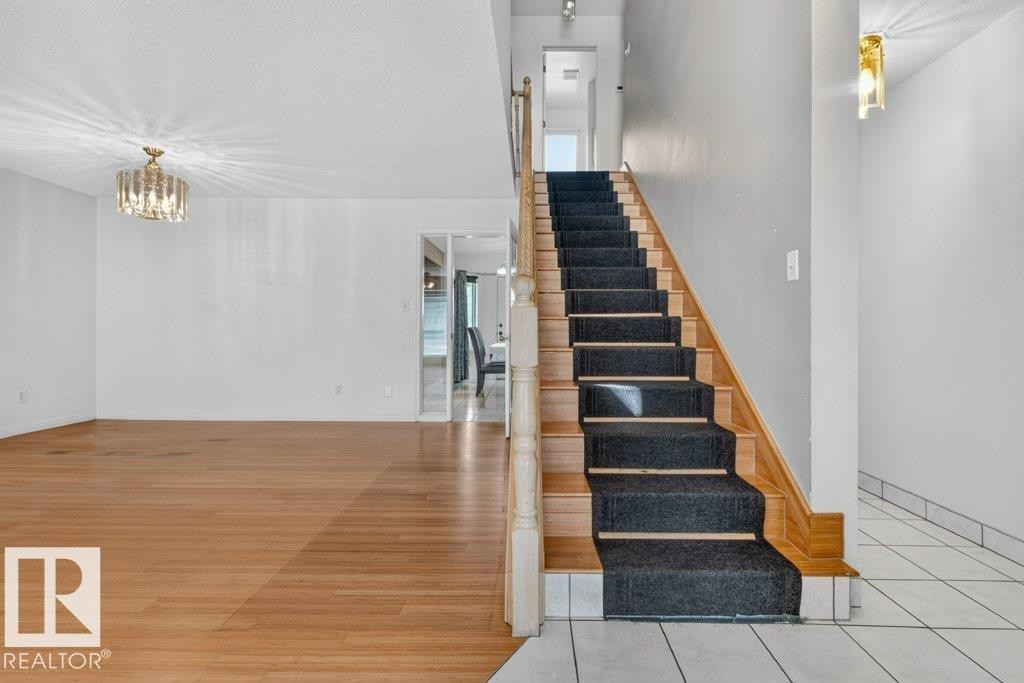 Wood-finish flooring and a crystal chandelier in the main living area - 16524 99 Street Nw, Edmonton, AB - Indoor Photo Showing Other Room