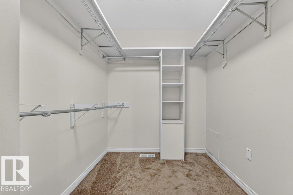 Walk-in closet featuring built-in shelving, hanging rods, and neutral-toned carpeting - 16524 99 Street Nw, Edmonton, AB - Indoor With Storage