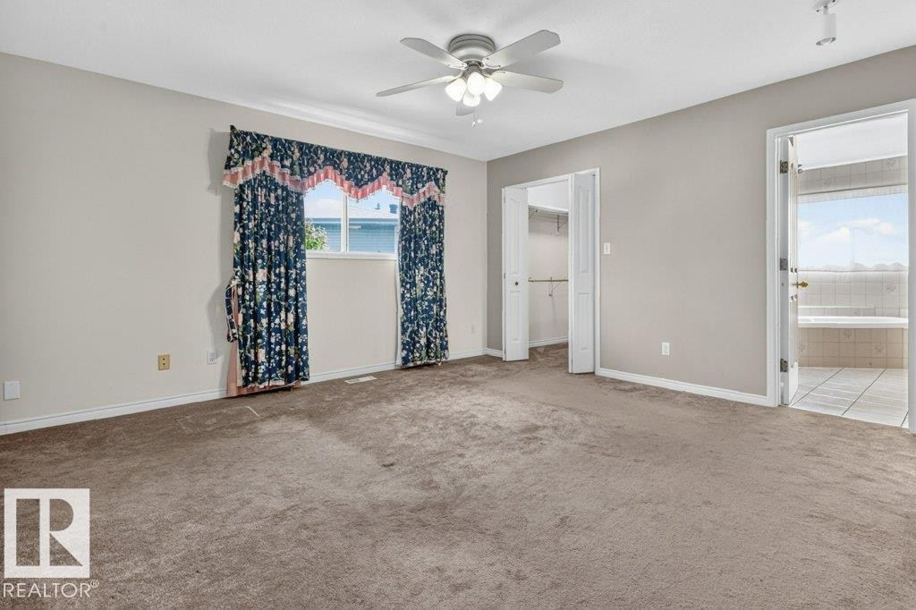Carpeted room featuring a ceiling fan with integrated lighting, a window with curtains, and two separate doorways - 16524 99 Street Nw, Edmonton, AB - Indoor Photo Showing Other Room