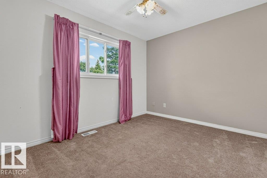 Bright upstairs bedroom 2 featuring a large window, neutral wall paint, white trim, and brown carpeting - 16524 99 Street Nw, Edmonton, AB - Indoor