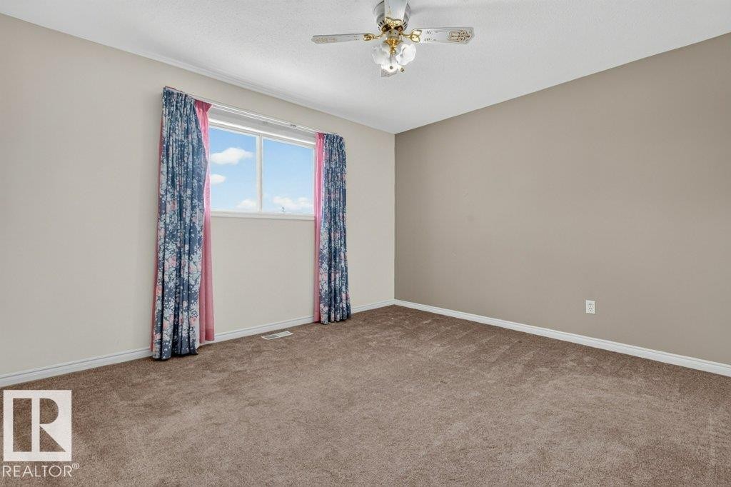 Bright upstairs bedroom 3 featuring light brown wall paint, a ceiling fan with integrated lighting, and neutral-toned carpet flooring - 16524 99 Street Nw, Edmonton, AB - Indoor Photo Showing Other Room