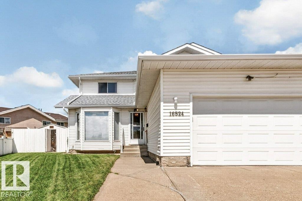 White vinyl siding exterior with an integrated garage, a bay window, a concrete walkway, and a manicured lawn - 16524 99 Street Nw, Edmonton, AB - Outdoor