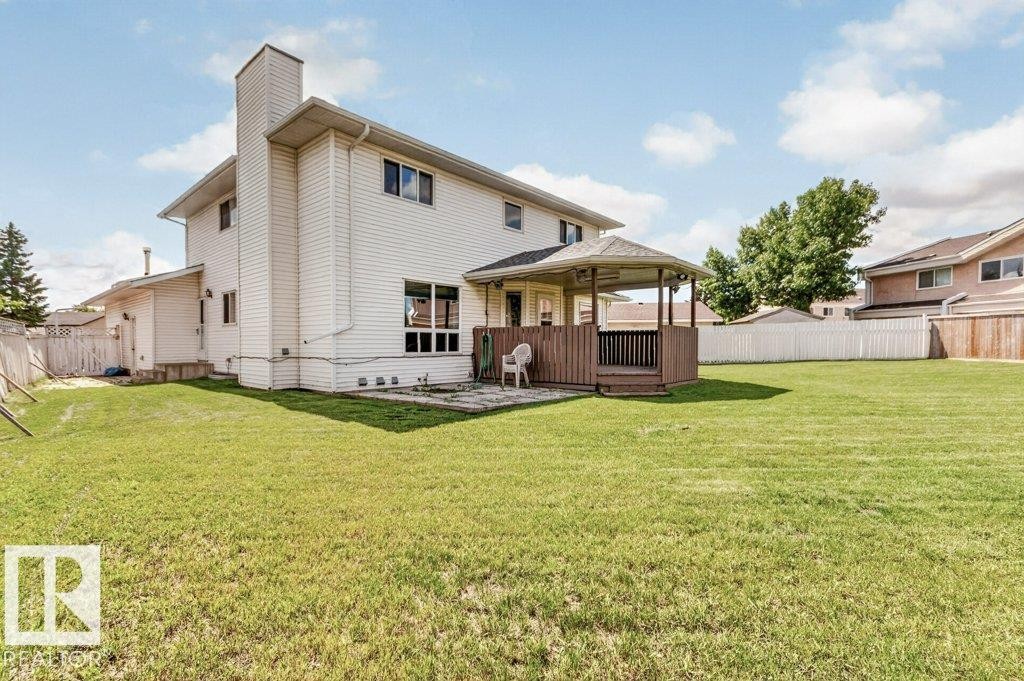 Expansive green lawn with a covered wooden deck, bordered by a wooden fence - 16524 99 Street Nw, Edmonton, AB - Outdoor With Deck Patio Veranda