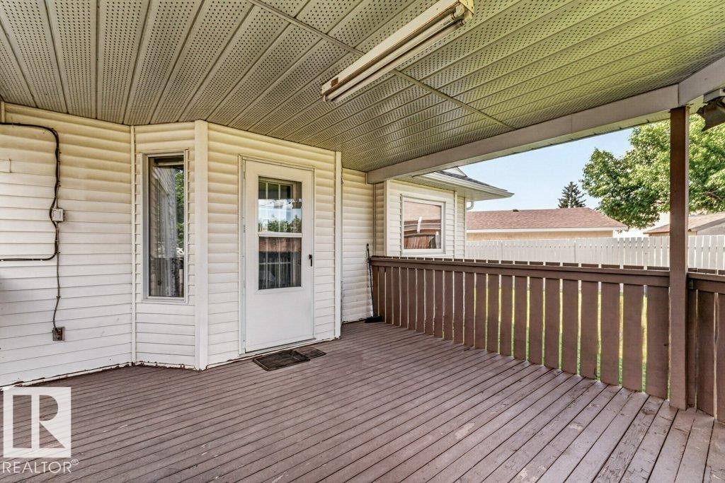 Expansive covered deck featuring wood-finish flooring, a white vinyl siding exterior, a white picket fence, and a transom window door - 16524 99 Street Nw, Edmonton, AB - Outdoor With Deck Patio Veranda With Exterior