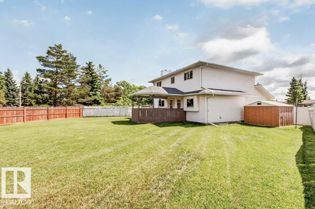 Expansive backyard featuring a manicured lawn, established perimeter fencing, mature trees, a covered patio area, and an outdoor storage shed - 16524 99 Street Nw, Edmonton, AB - Outdoor