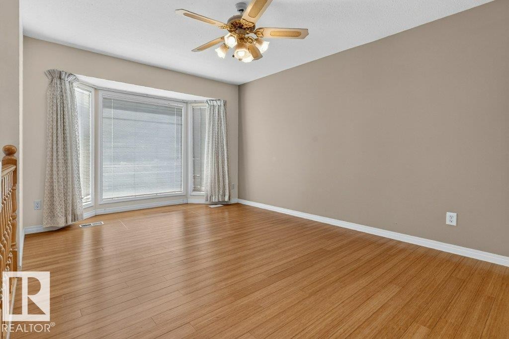 Spacious room featuring a prominent bay window, wood-finish flooring, a ceiling fan with integrated lighting, neutral wall tones, and white trim - 16524 99 Street Nw, Edmonton, AB - Indoor Photo Showing Other Room