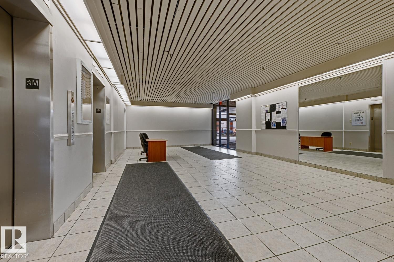 Spacious corridor featuring white tiled flooring, a slatted ceiling, and recessed lighting - 505 10145 109 Street, Edmonton, AB