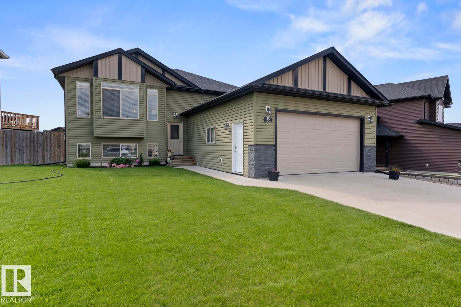 Green siding exterior with black trim accents and a contrasting light-colored garage door - 35 Falcon Road, Cold Lake, AB