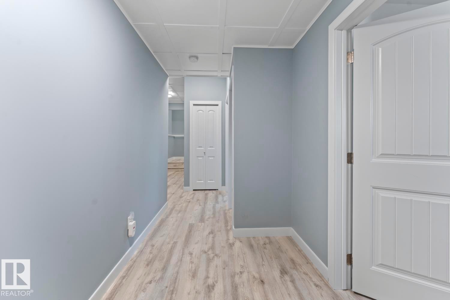 Hallway featuring wood-finish flooring, light blue wall paint, white baseboards, and white ceiling panels - 35 Falcon Road, Cold Lake, AB