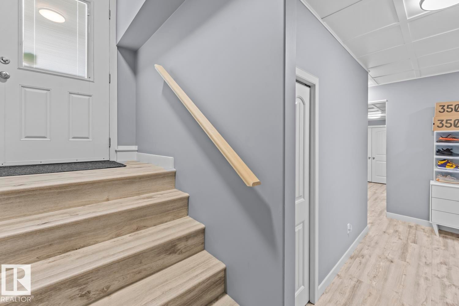 Entryway featuring wood-finish flooring on stairs and hallway, a white paneled door with glass insert, a light wood handrail, and light gray wall paint - 35 Falcon Road, Cold Lake, AB