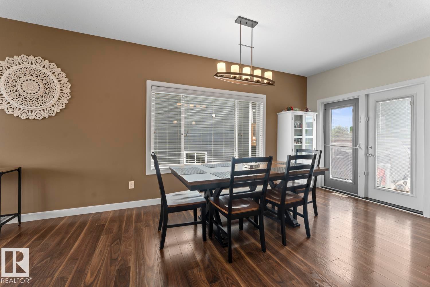 Dining area featuring wood-finish flooring, a contemporary linear chandelier, ample natural light from the large window, and double glass-panel doors - 35 Falcon Road, Cold Lake, AB